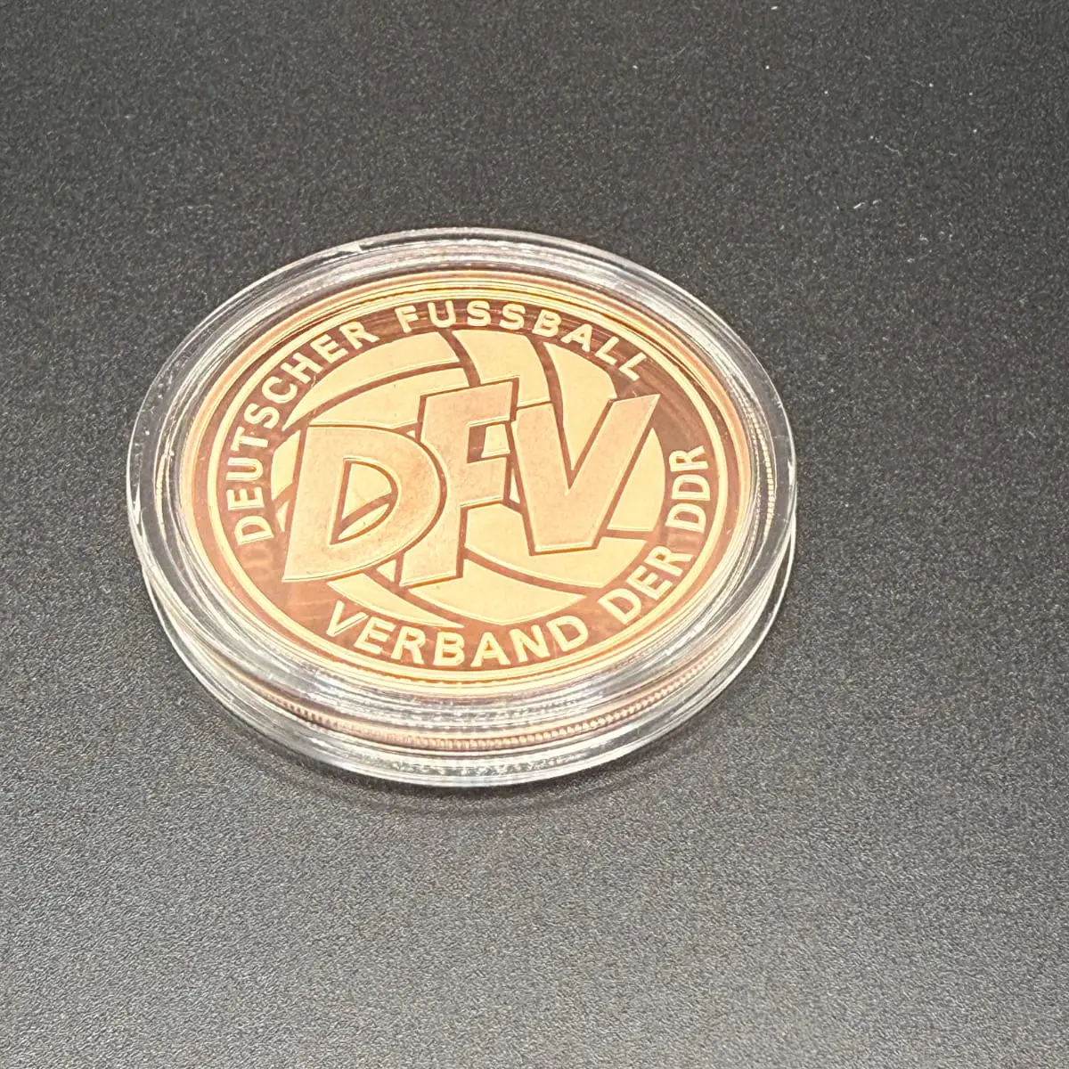 Fotografie der Medaille in ihrer Schutzkapsel, Rückseite mit DFV-Emblem, auf dunklem Grund